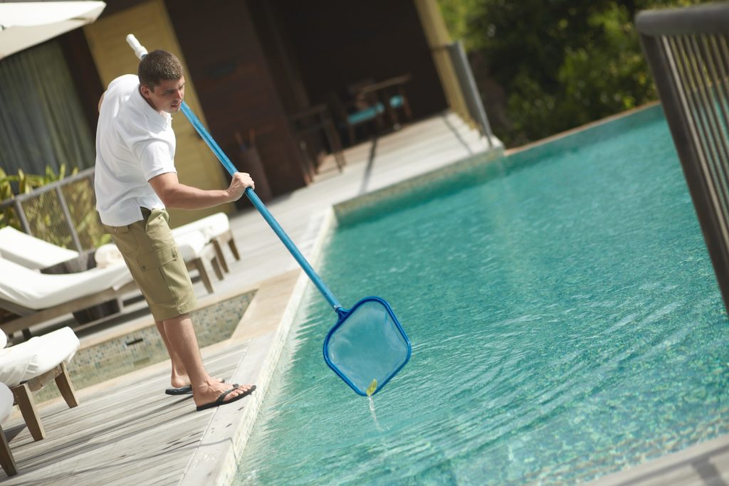 Swimming pool cleaner during his work at tropical villa. Professional cleaning service at work. Private property service.